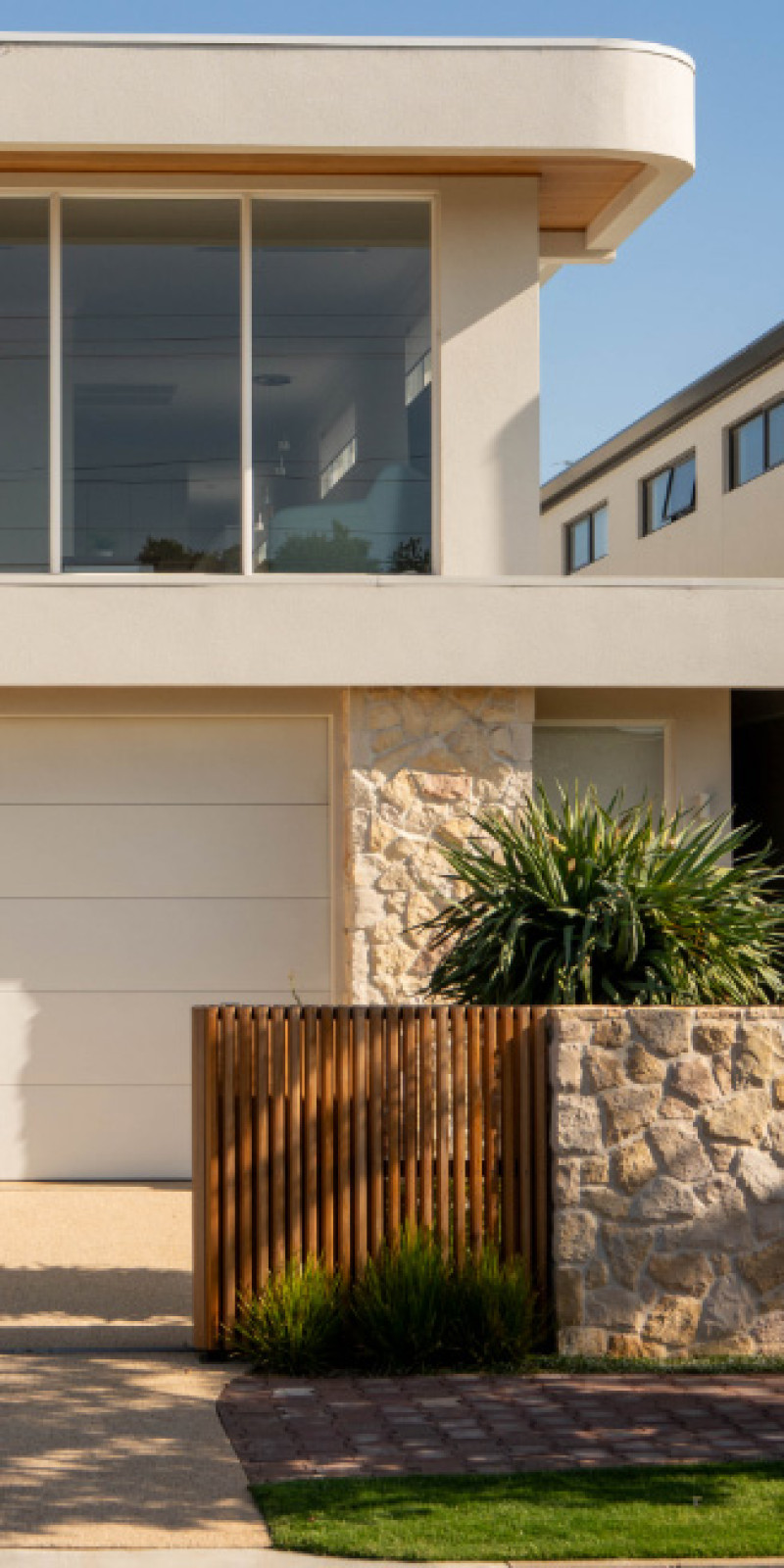 The front of a contemporary home with a curved roofline, stone wall and timber gate