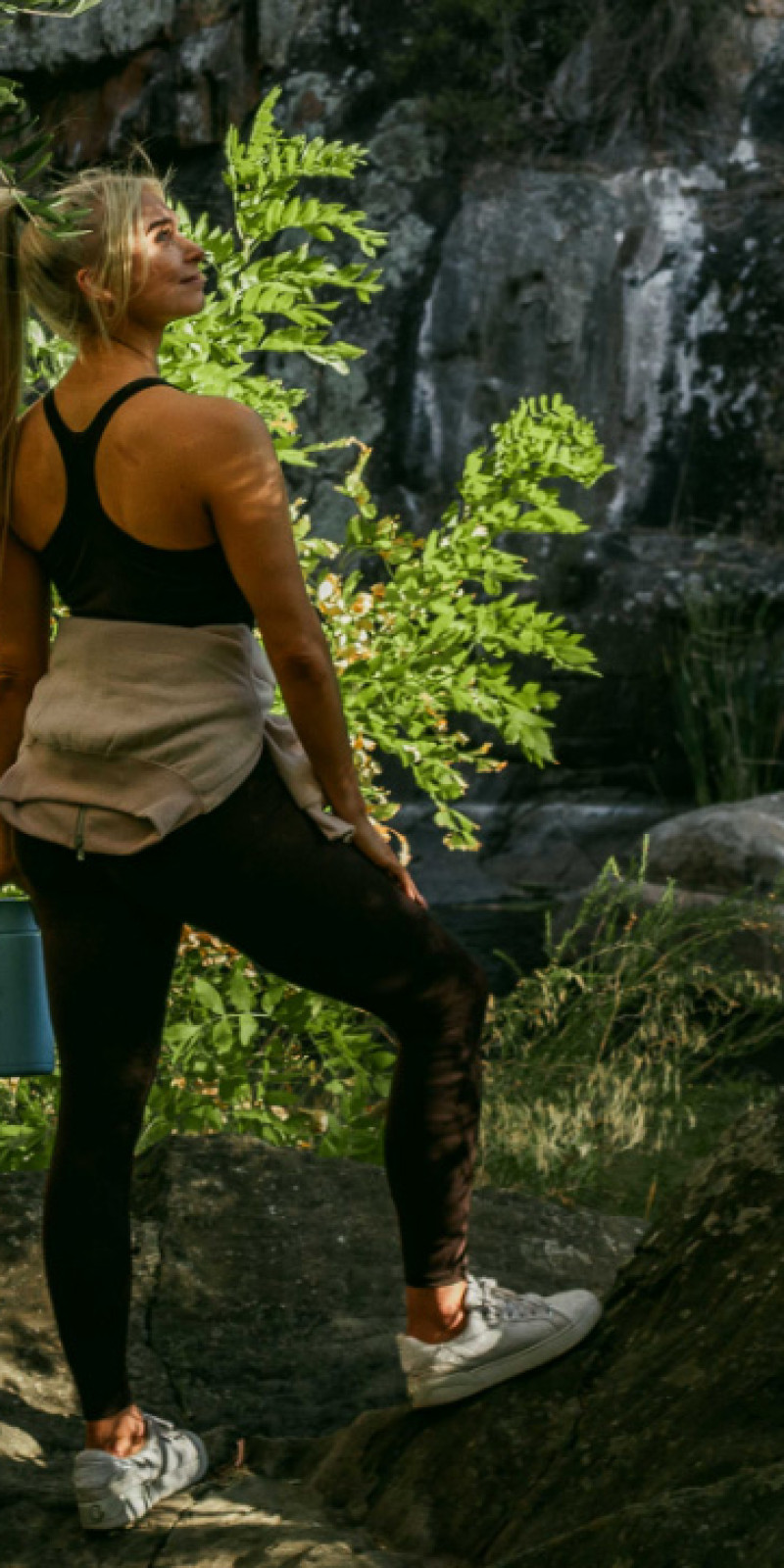 A woman in activewear standing on rocks below a cliff face in bushland