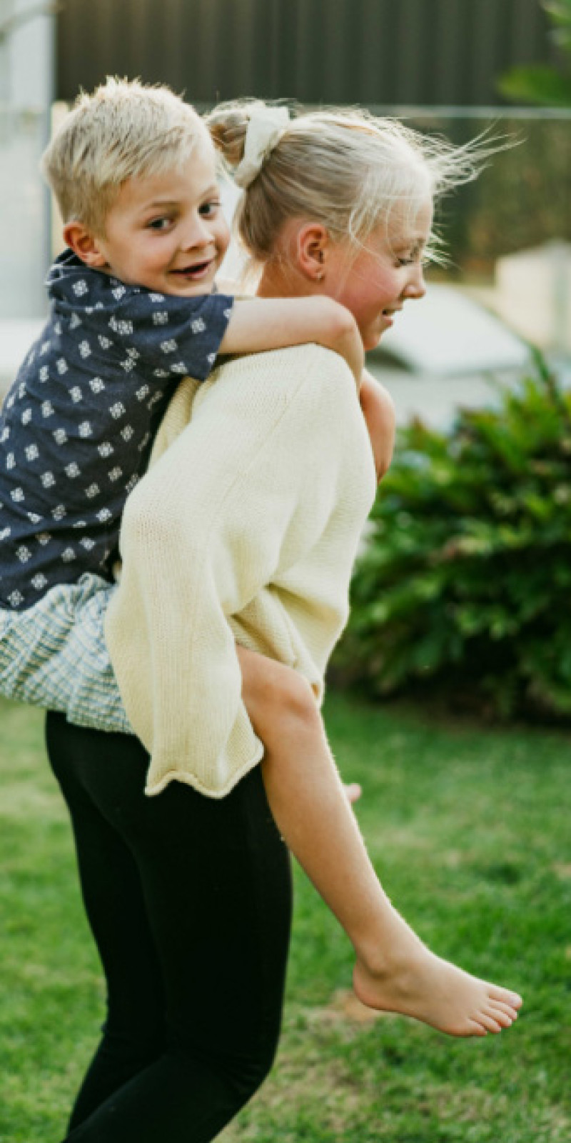 A girl carrying a boy on her back across a lawn