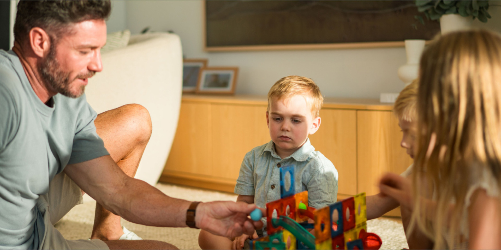 A father and two young children playing with building blocks in a living room
