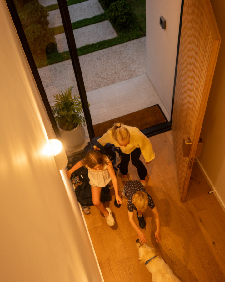 Children and a labrador greeting each other at an open front door, seen from the landing above