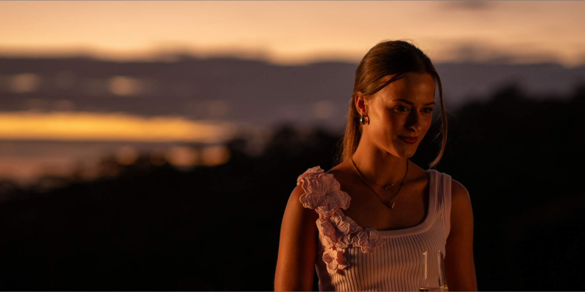 A woman standing outdoors at dusk with hills behind her