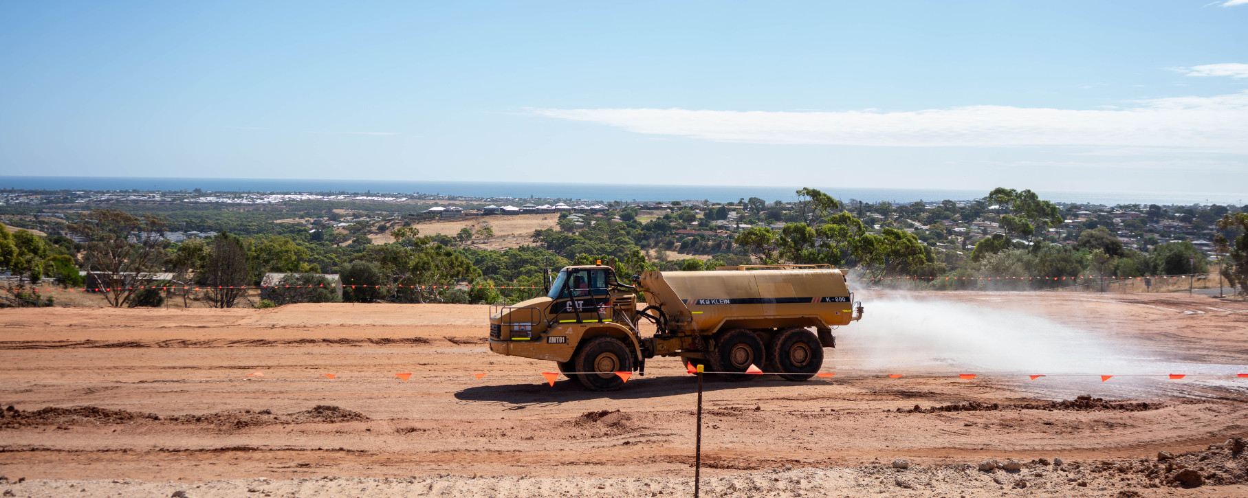A water truck damping down a graded construction site at Edenridge, with the coastline in the distance